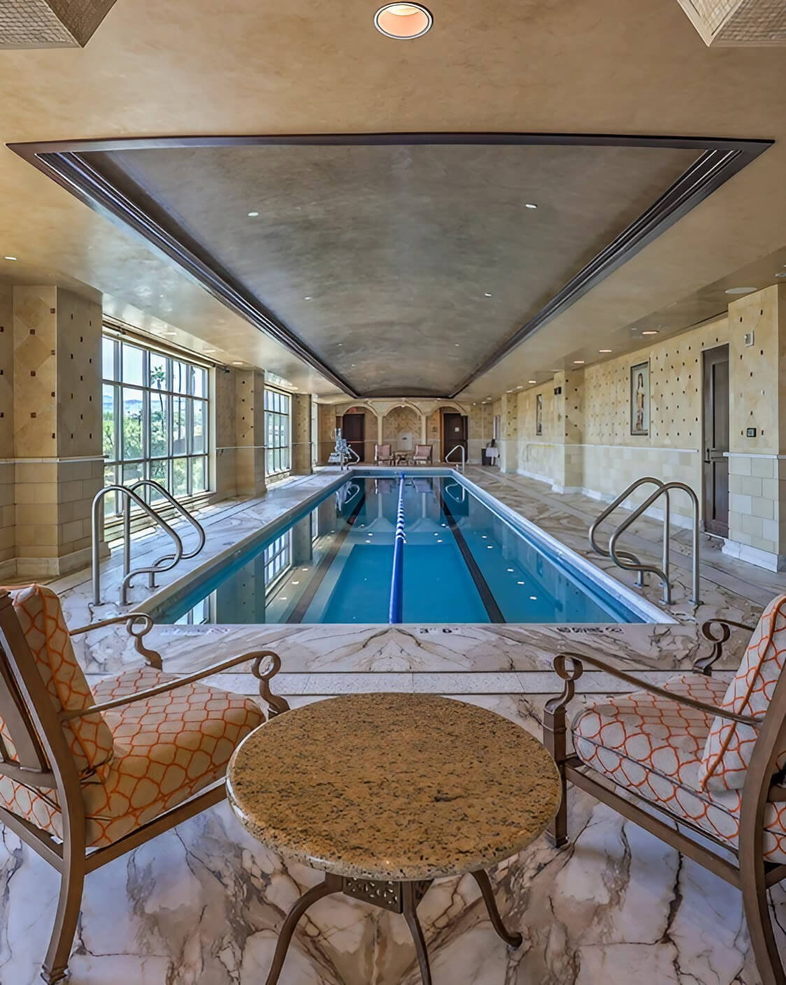 An elegant indoor pool surrounded by marble floors in a spacious home, showcasing luxury and tranquility.