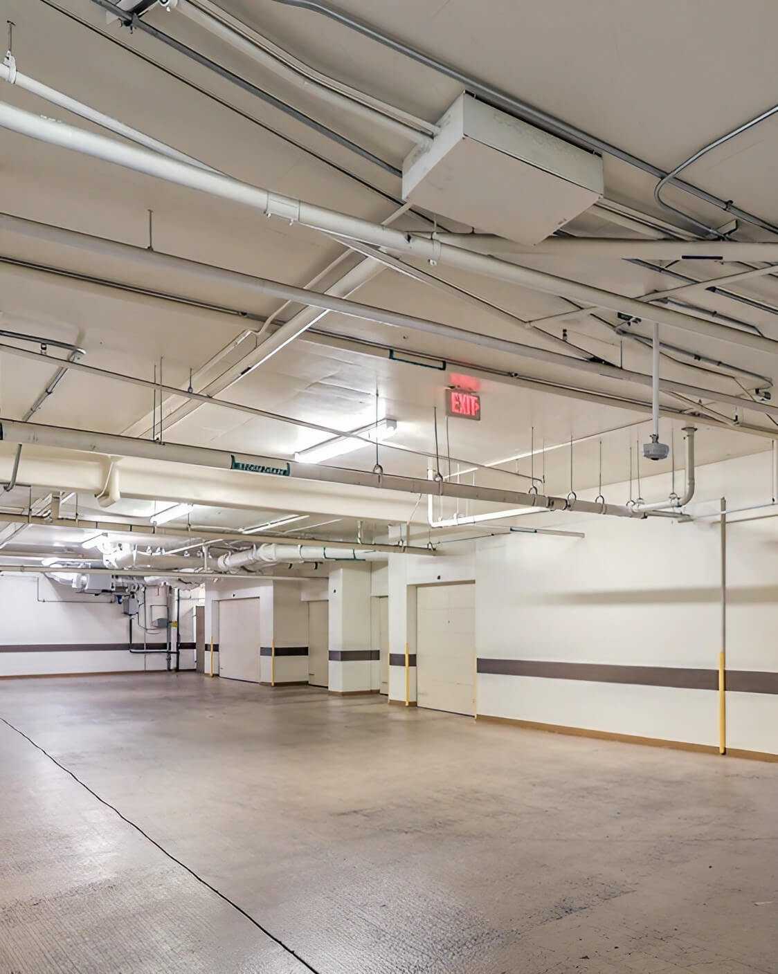 An unoccupied garage showcasing a large ceiling and a multitude of pipes running along the walls and overhead.